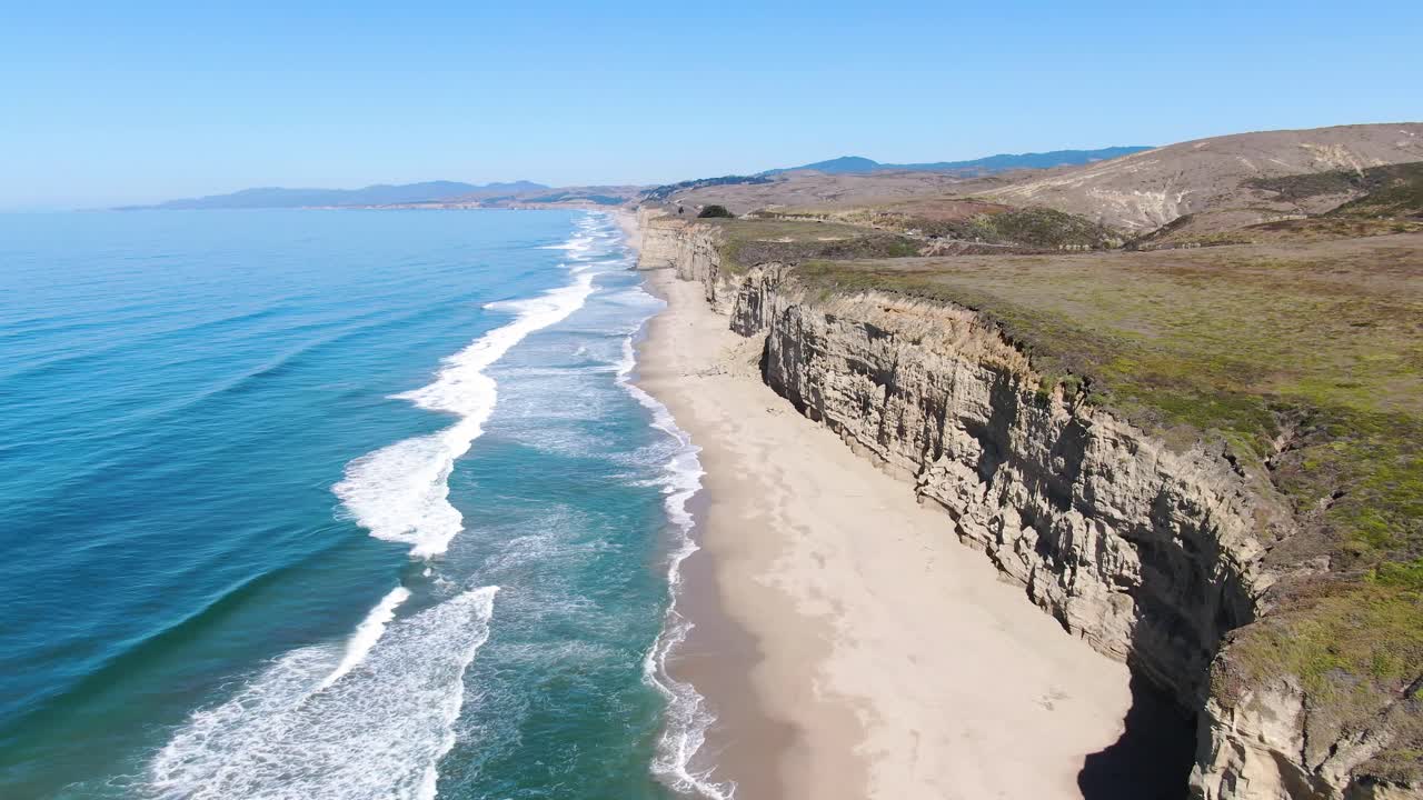 Aerial video shoot of Pescadero Coast shore that goes all over the horizon, along with the sea on the left and cars by the road in San Mateo, California
