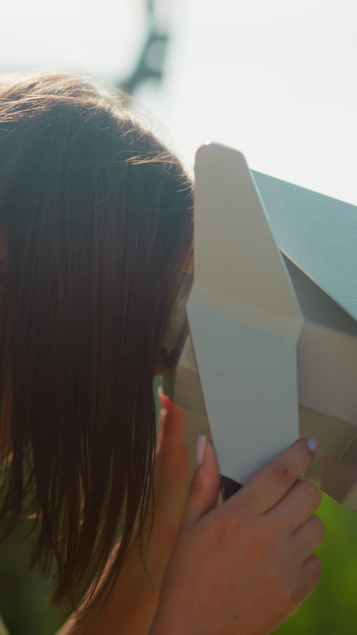 mujer concentrada disfruta de la vista mirando a través de binoculares turísticos instalados en la cubierta de observación contra los teleféricos en movimiento. mayor visibilidad cámara lenta