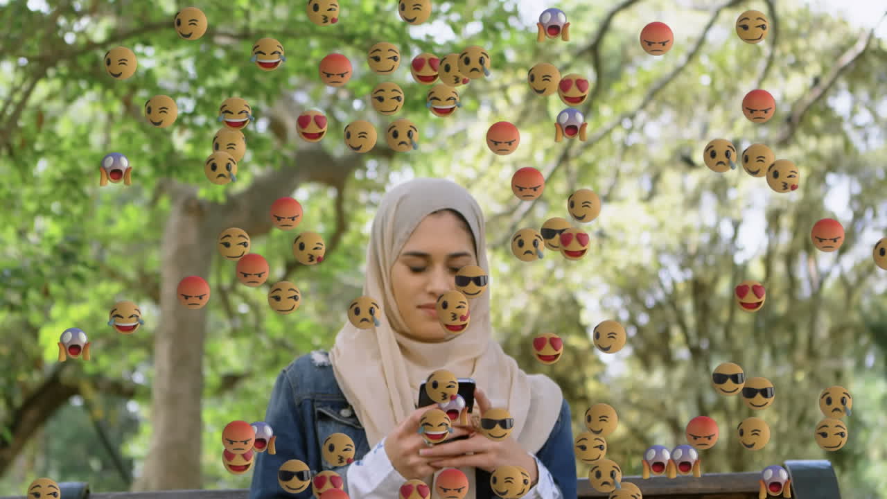스마트폰을 사용하여 히자브를 입은 여성 위에 떨어지는 이모티콘의 애니메이션
