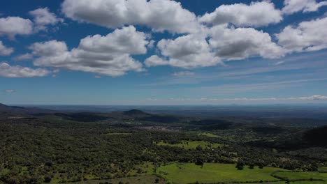 flight-where-the-filming-divides-the-blue-sky-with-clouds-and-the-other-the-horizon,-a-plain-with-a-distant-vision-nearby,-small-oak-forests-and-green-meadows-appear-in-spring-Toledo-Spain