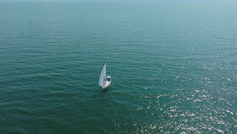 Luftaufnahme-Eines-Weißen-Segelboots-Im-Ruhigen-Meeresmeer,-Weiße-Segelyacht-Mitten-Im-Grenzenlosen-Meer,-Sonniger-Sommertag,-Weite-Umlaufende-Aufnahme