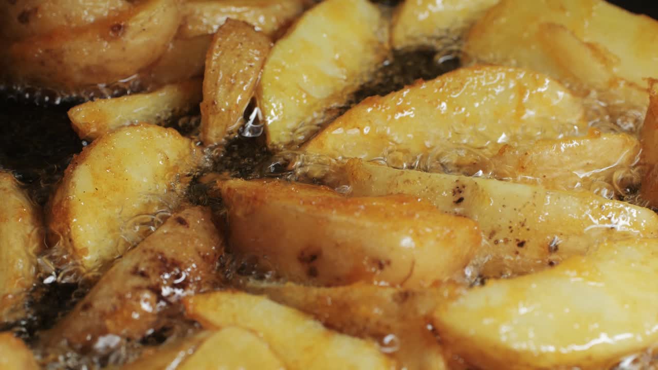 Making fried potato wedges, country potatoes in a pan in boiling oil close-up. Potato pieces snack food. Chef cooking in cafe kitchen. High quality 4k footage