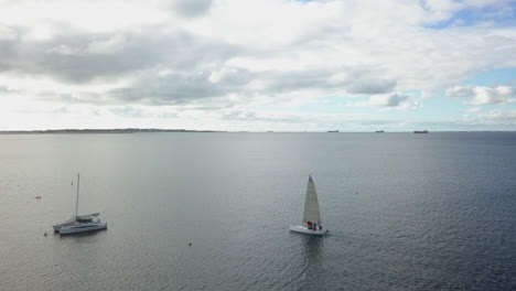 Sailboat-approaches-moored-catamaran-on-calm-ocean-day