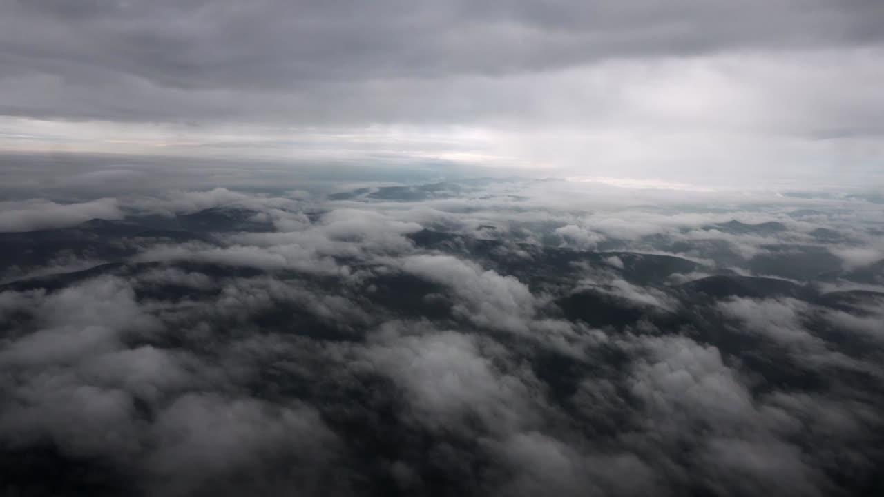 Flying across Germany, the aircraft soars over fog-covered hills beneath heavy overcast. Mist drifts across the rolling terrain, creating a dramatic and atmospheric view of the countryside from above