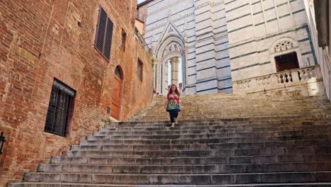 a young lady walks down the steps leading from the medieval siena cathedral, siena, italy