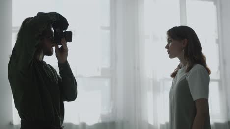 photographer taking pictures of young pretty woman beside window in room