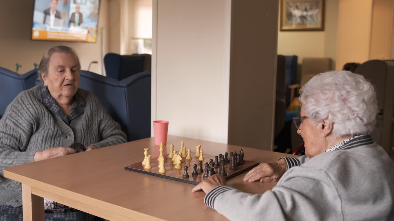 Senior women playing chess at table in canteen at nursing home