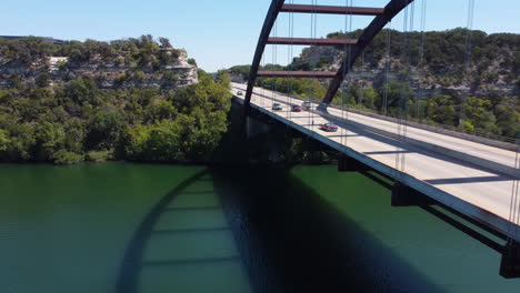 an aerial shot captures the iconic pennybacker bridge in austin, texas, with cars driving across it, showcasing the beautiful landscape and water below.