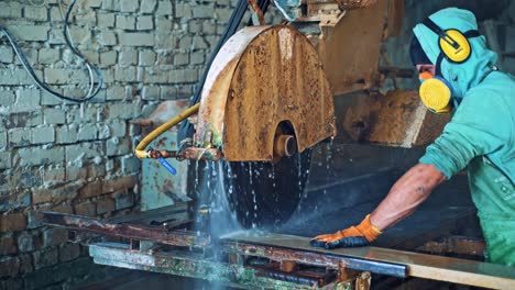 worker in uniform with protective mask puts the big stone slab into the cutting machine.