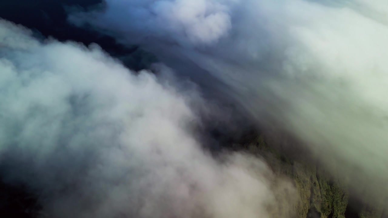 Tiefe Wolken ziehen bei hellem Tageslicht über Berge, enthüllen einen grünen Bergrücken darunter und schaffen dynamische Drohnenaufnahmen einer Wolkenlandschaft.