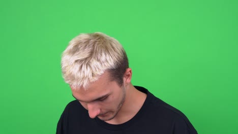 handsome guy with dyed blond hair and three-day stubble in black t-shirt touches nose posing for camera on chromakey closeup