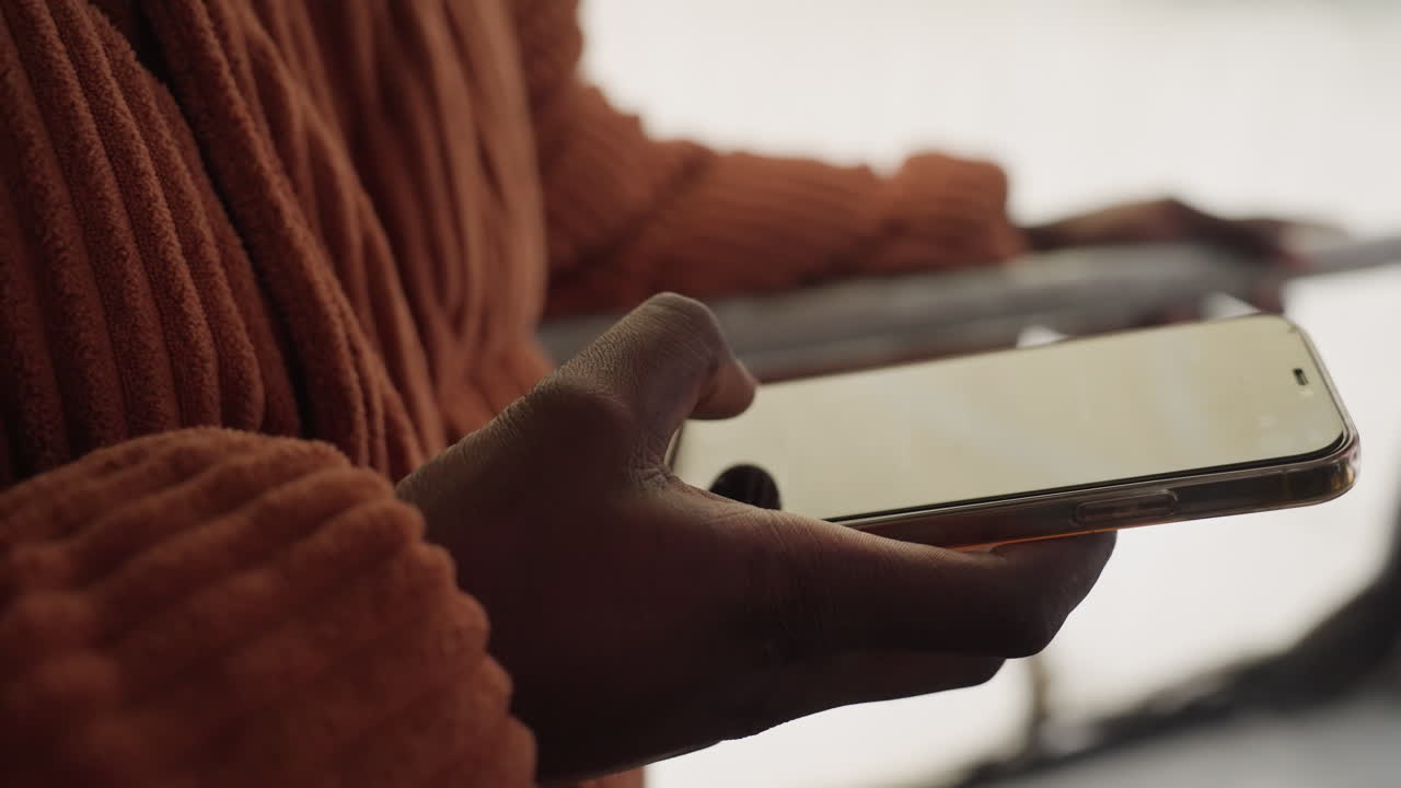 Mani di colore che controllano il telefono all'interno dell'autobus vicino al corrimano, maglione di lana color ruggine, che toccano le app, bagliore di notifica, finestrino nuvoloso, pendolarismo urbano dinamico, risposte rapide, produttività in movimento.