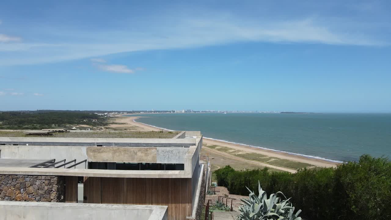 Panoramic aerial view revealing coastal city nestled along sandy shoreline, with pristine beach stretching beneath clear azure sky and tranquil ocean horizon
