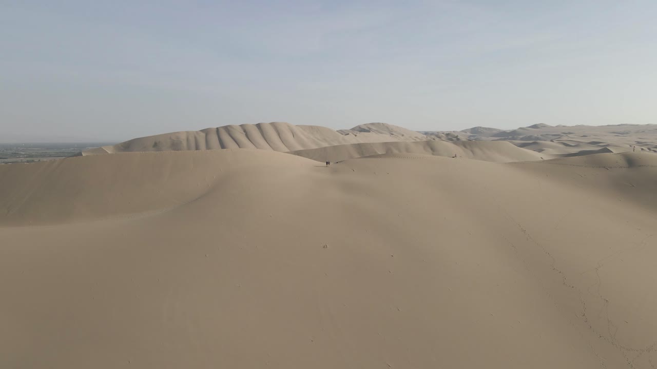 vuelo aéreo hacia tres personas en la cima de una enorme duna de arena en ica, perú