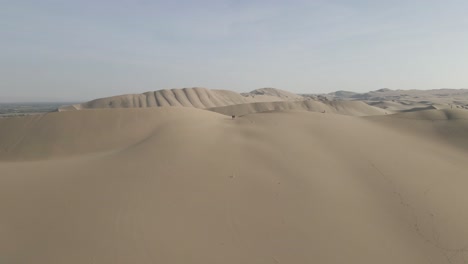 vuelo aéreo hacia tres personas en la cima de una enorme duna de arena en ica, perú
