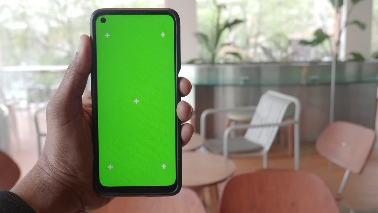 mano sosteniendo un teléfono inteligente con pantalla verde en un café