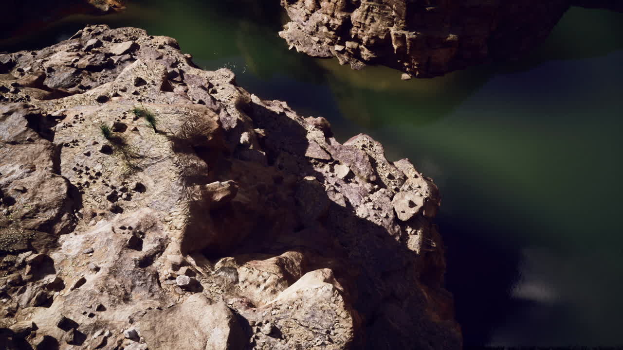 Scoscese pareti rocciose erose adiacenti a una pacifica superficie liquida luminosa.