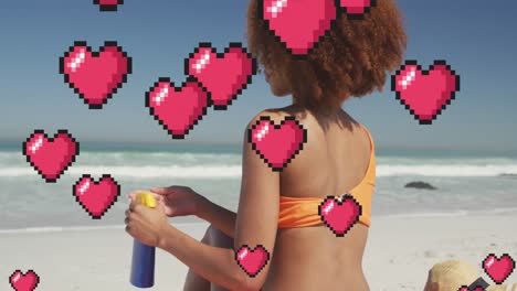 animación de iconos digitales de corazón sobre una mujer aplicando crema solar en la playa