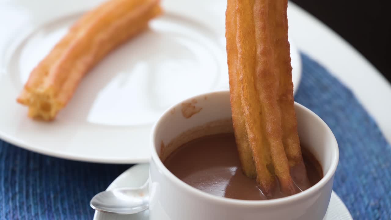 un metraje en cámara lenta sumergiendo churros españoles en salsa de chocolate caliente