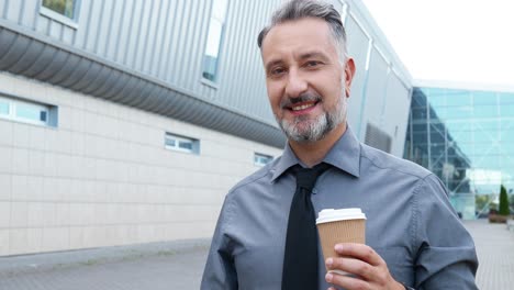 close-up view of gray-haired businessman holding coffee cup and looking at camera in the street