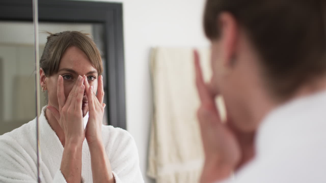 중년 백인 여성이 집 화장실에서 피부 관리법을 적용합니다.