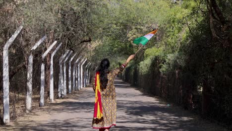 young girl waving the indian tricolor national flag at remote location at day from back angle