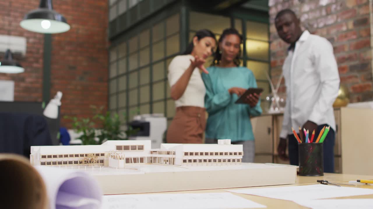 Happy diverse architects looking at architectural models and using tablet at office