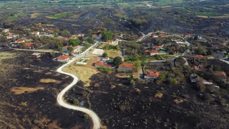 Dramatic-aerial-of-a-village-surrounded-by-burned-land-in-the-aftermath-of-a-wildfire-in-northern-Greece,-August-2023