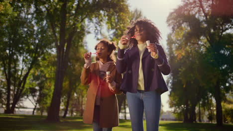 joyful family blowing soap bubbles standing in green park. happy leisure time.