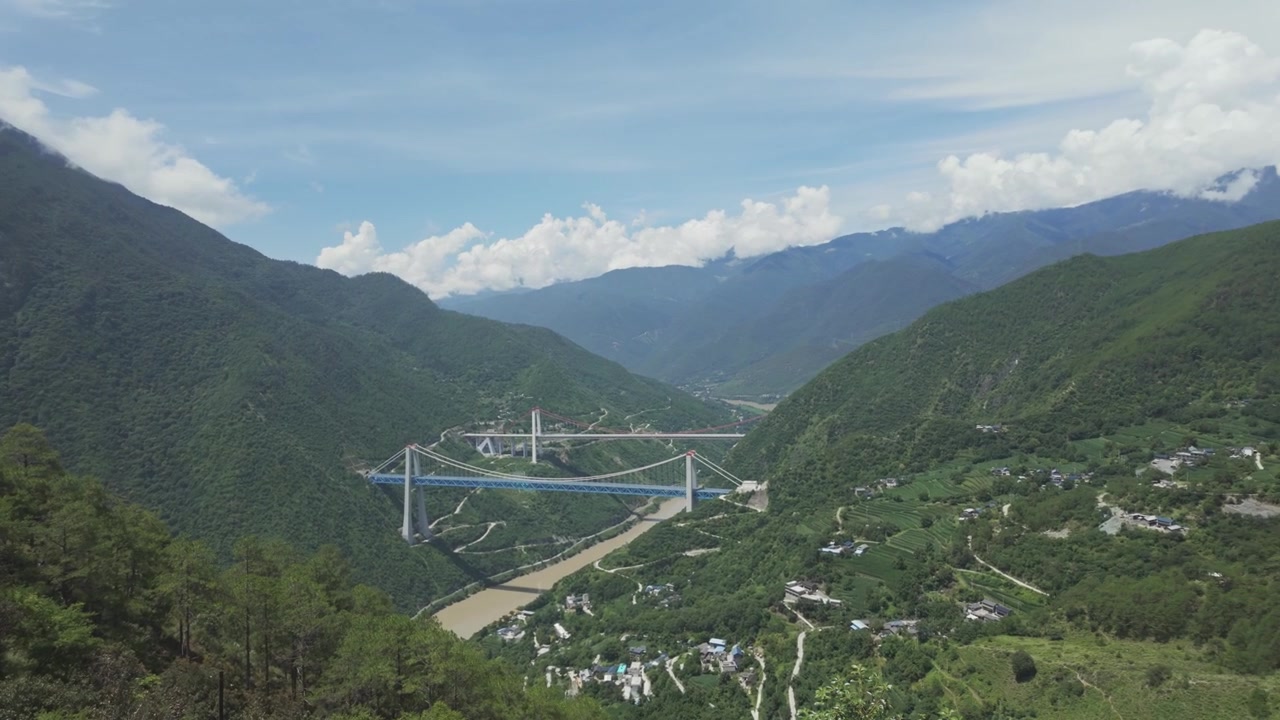 Một cảnh quay rộng mang tính điện ảnh về cây cầu treo khổng lồ bắc qua sông Kim Sa tại Hẻm núi Hổ Khiêu, thể hiện kỹ thuật xây dựng ấn tượng và phong cảnh núi non hùng vĩ.