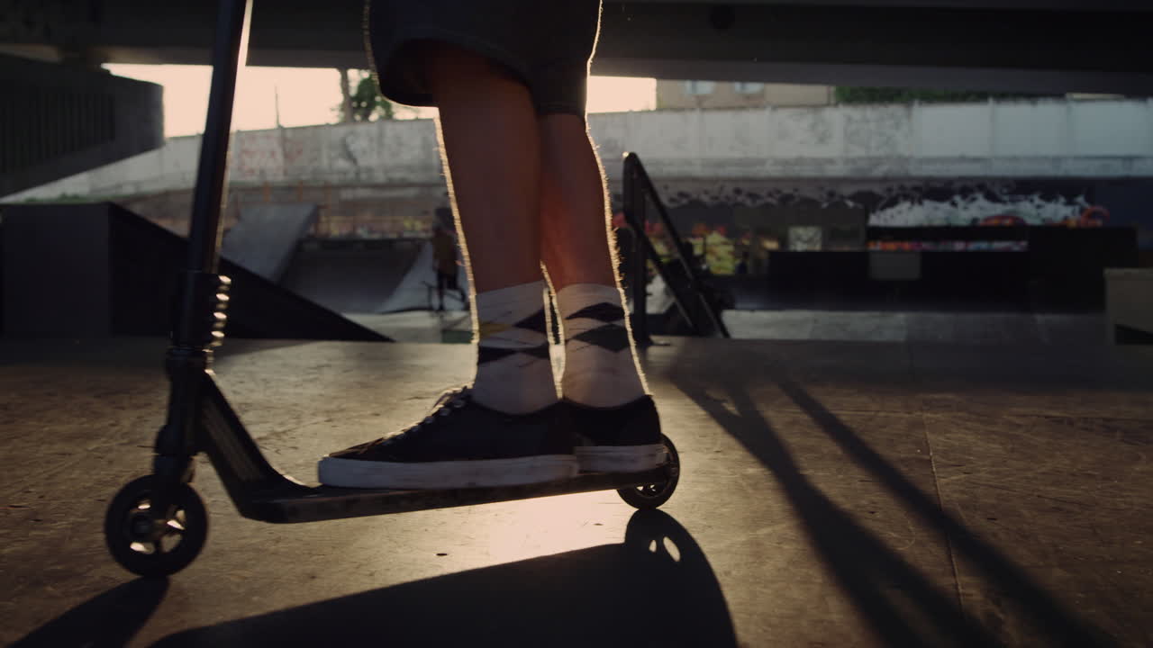 Active scooter rider practicing on ramp at urban skate park. Man legs on scooter