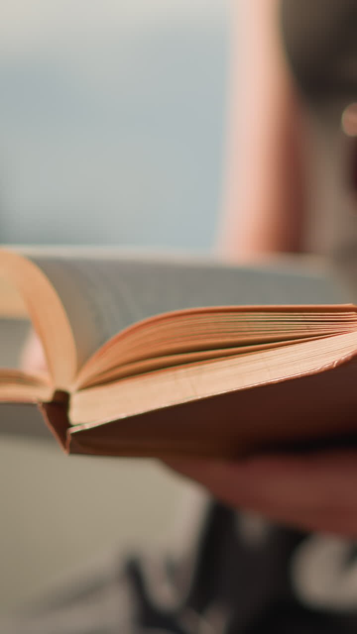 Close-up of individual holding a brown book cover with fast-flipping pages to the right,sunlight illuminates the book while the background remains blurred
