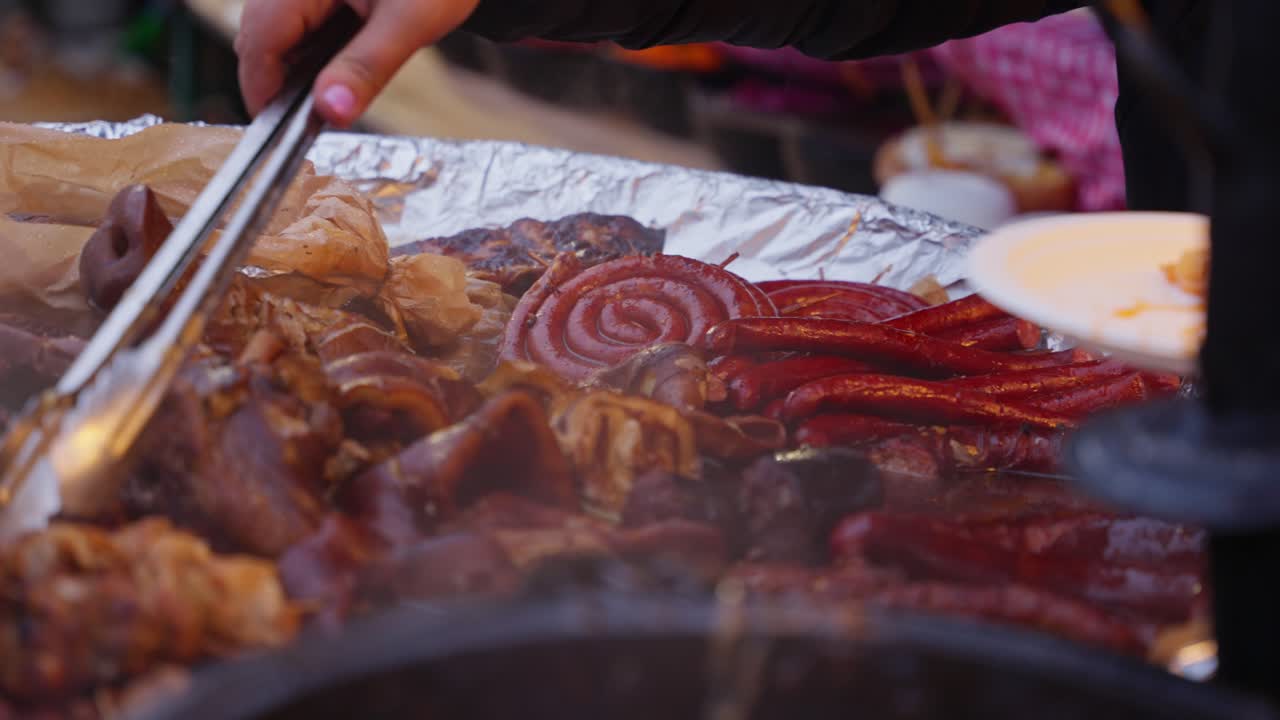 Cuoco di strada che prepara porzioni di carne alla griglia e le impiattata da una superficie calda per i clienti che raccolgono le carni con le pinze