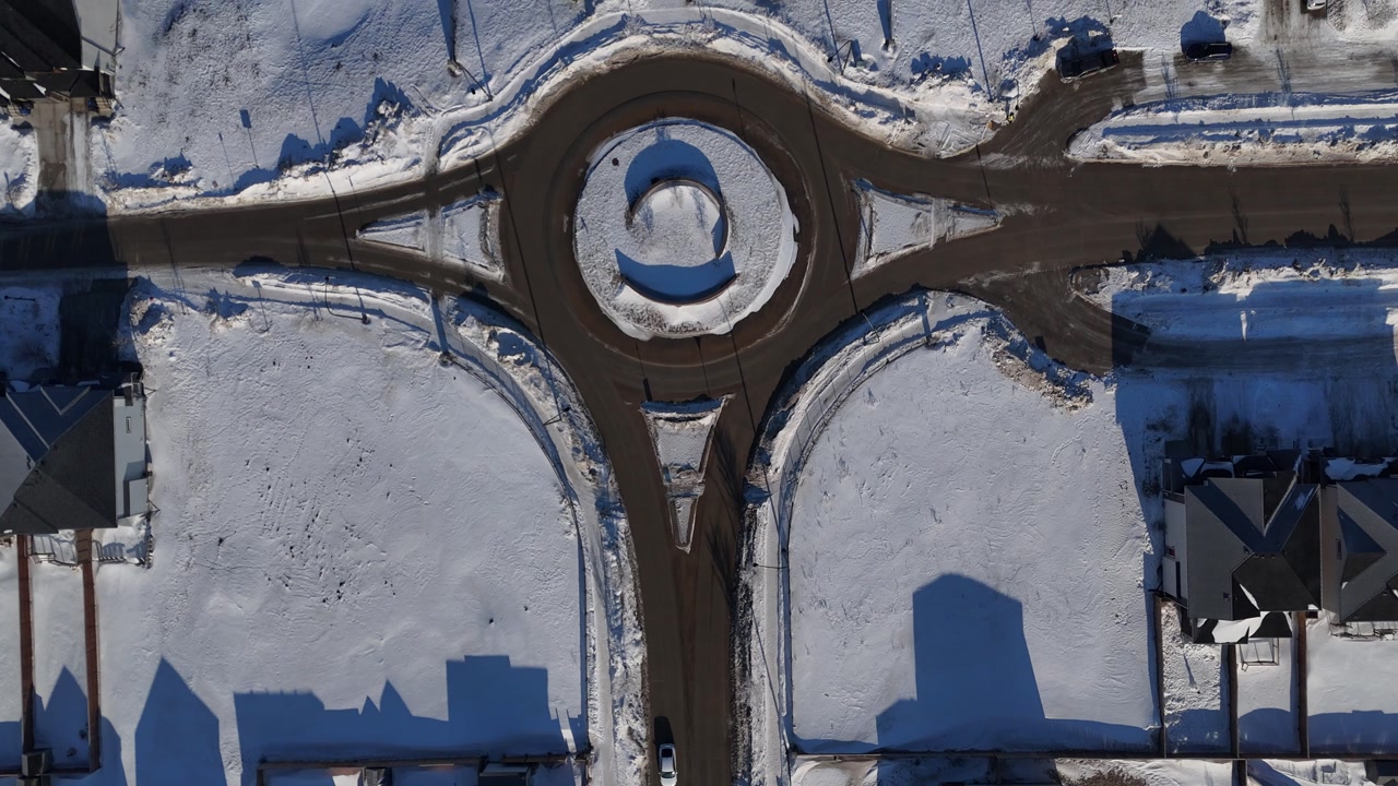 Overhead aerial drone shot of residential street and roundabout in Bridgwater Winnipeg Manitoba. Snow covered houses, yards, and cars on road during a sunny winter day.