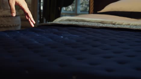 hand touching a navy blue quilted comforter on a bed.