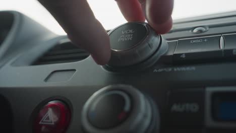 close up of person pressing volume push button and turning audio control knob on car dashboard highlighting finger interaction with media dial and rotary control in vehicle interior