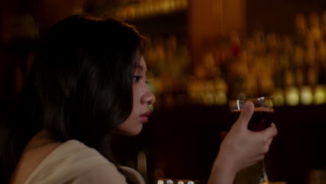 woman holding a glass in a dimly lit bar, reflecting on her thoughts