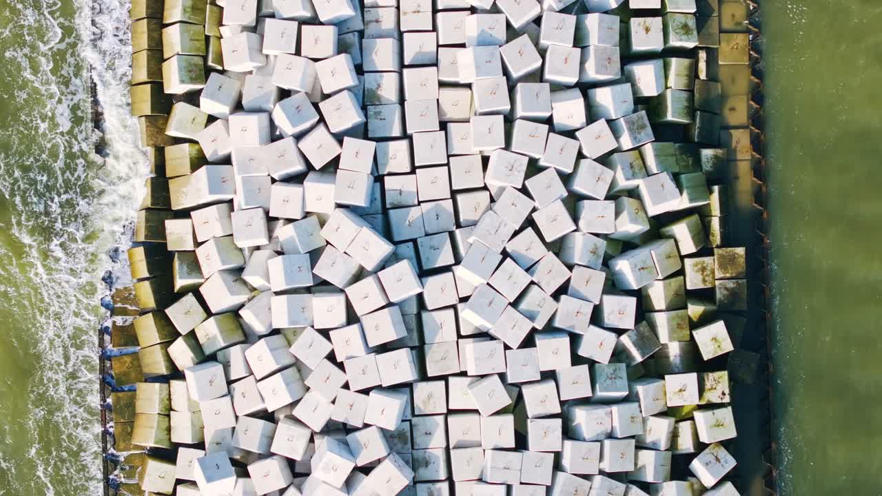Top down backward flight reveals geometric breakwater structure in sea, Liepaja