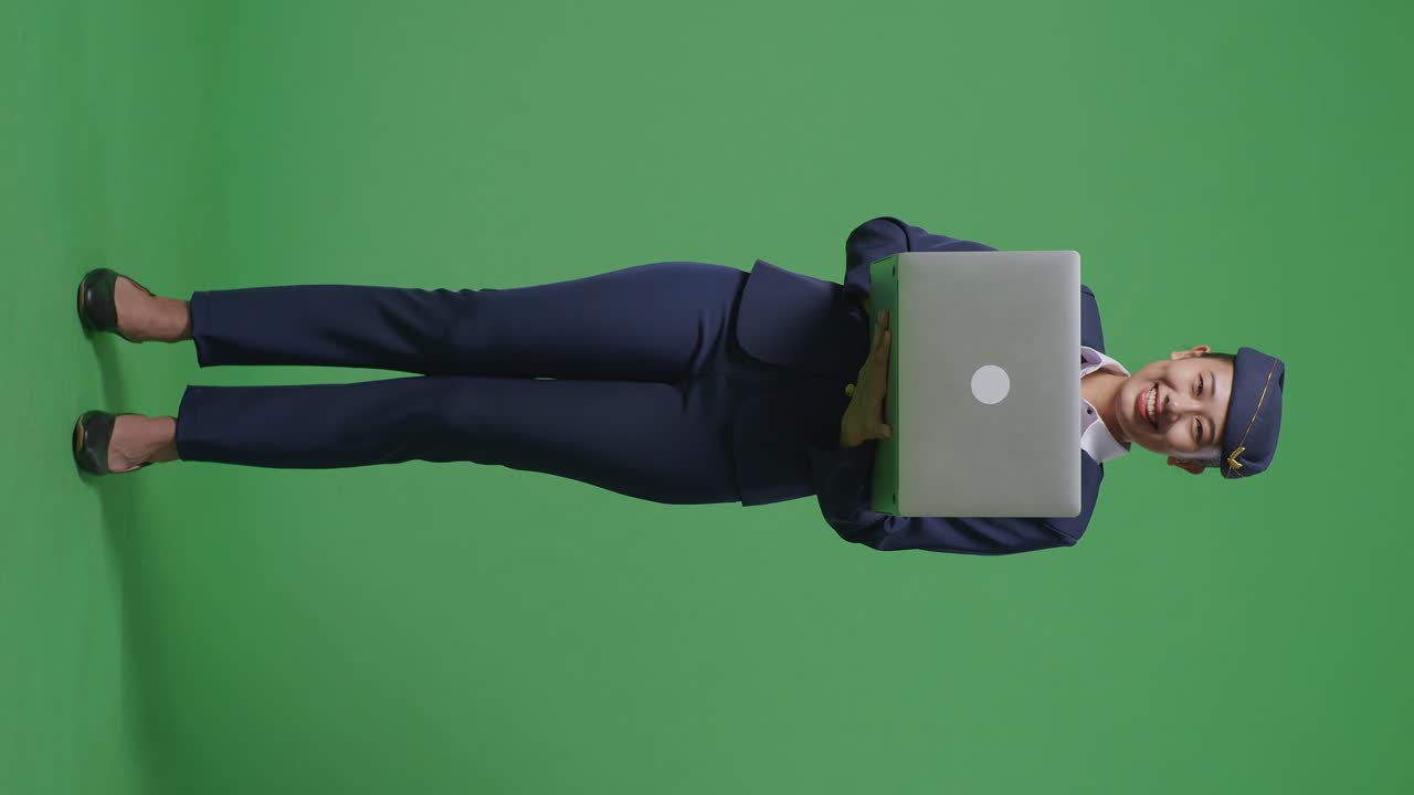 cuerpo lleno de azafata asiática usando una computadora portátil y apuntando a un lado mientras está de pie en el estudio de fondo de la pantalla verde