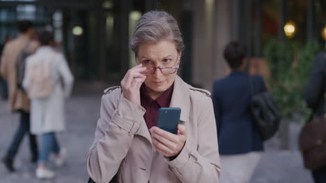 portrait successful mature caucasian woman using smartphone in city enjoying texting browsing online messages on mobile phone wearing glasses slow motion