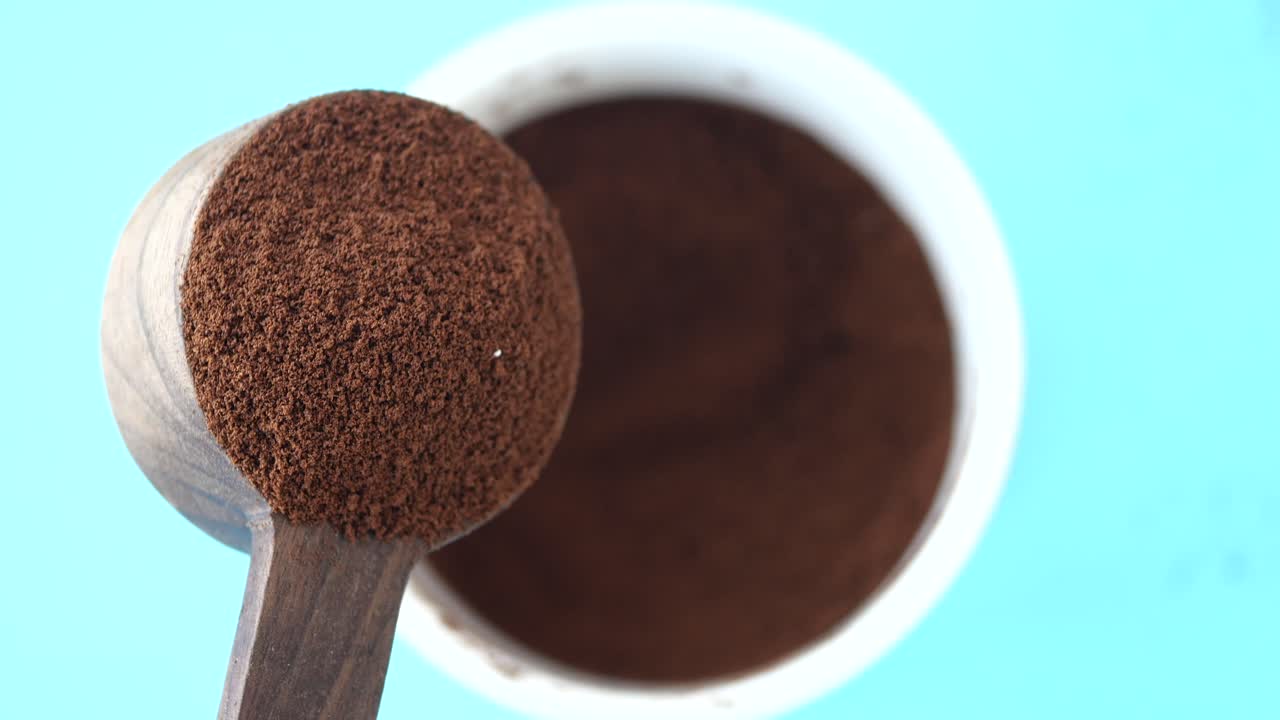 Close up of wooden spoon pouring ground coffee into white cup