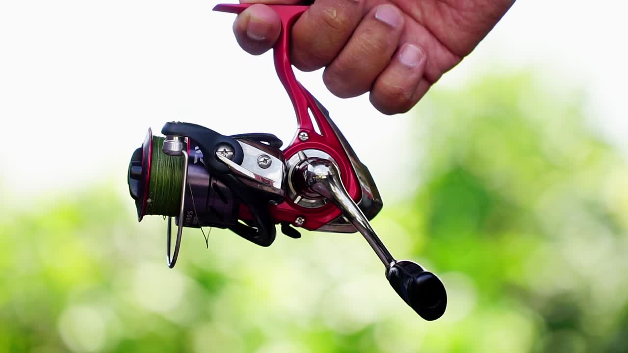 Hand is holding spinning reel showing on the camera with nature blur background
