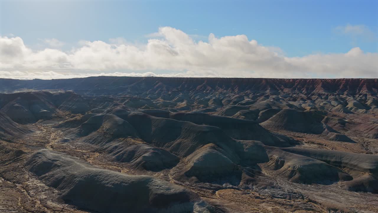 A breathtaking drone aerial view captures the Painted Desert in the Southwest. Vibrant colored hills and geological strata stretch across the vast high desert landscape under a clear sky