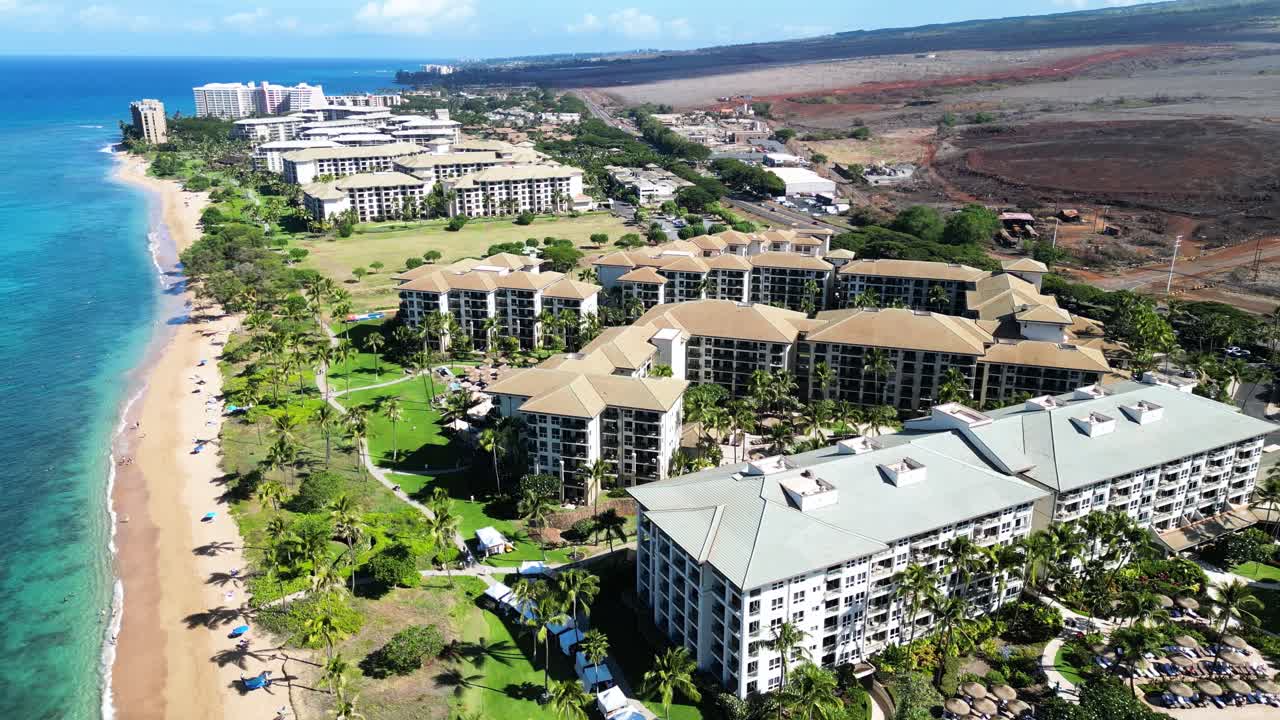 Aerial pan reveals Maui’s resort shoreline with hotels, palms, beach, and ocean