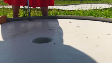 woman in summer dress putting ball into hole in mini golf field, close up