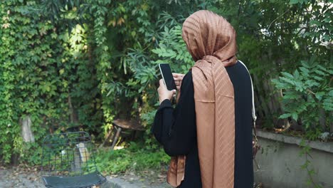 woman wearing hijab and abaya looking at smartphone outdoors