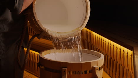 pouring water into a wooden sauna barrel