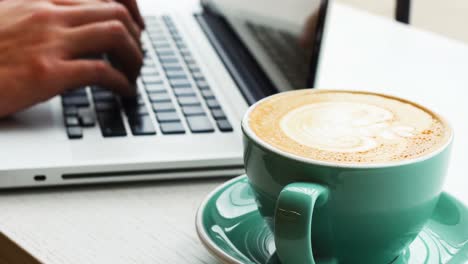hombre usando una computadora portátil mientras bebe café