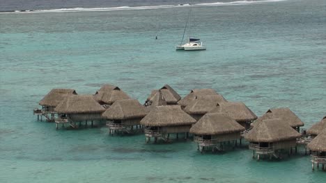 Casas-De-Madera-Sobre-El-Agua-Y-Un-Yate-En-La-Laguna-Azul-En-Moorea,-Polinesia-Francesa