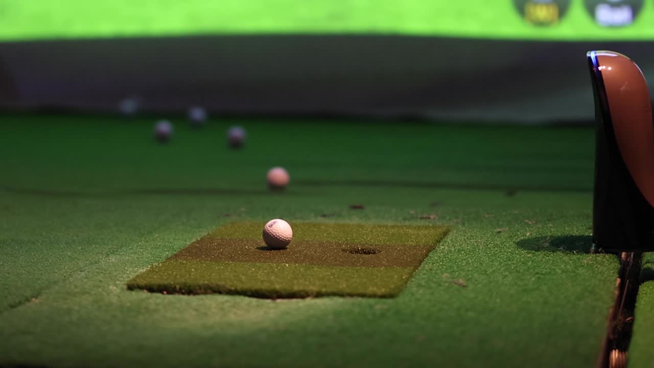 A detailed view of a golf ball on a mat in an indoor setting, focusing on the ball's position and surroundings.